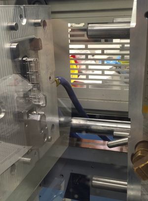 An injection molding machine opens to reveal a cleat plastic molding